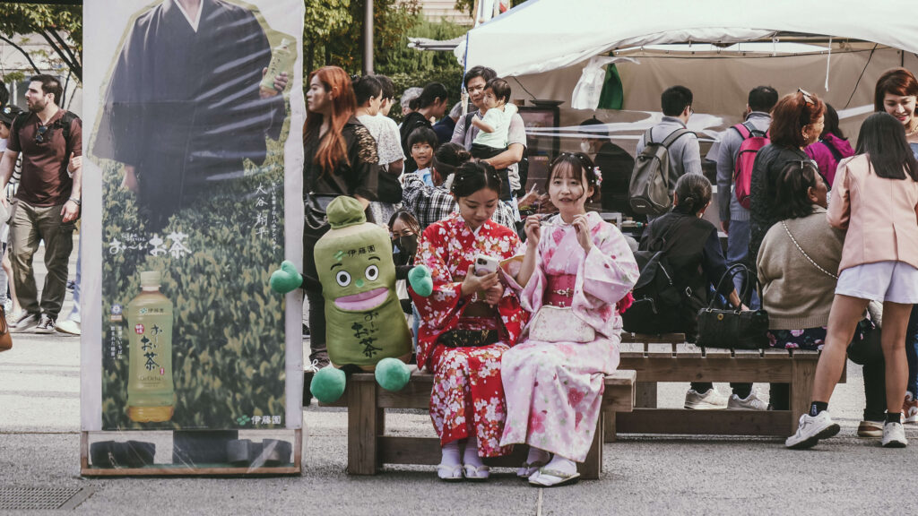 Deux jeunes femmes en kimono assises devant le temple d’Asakusa à Tokyo, entourées d’une ambiance festive et traditionnelle.