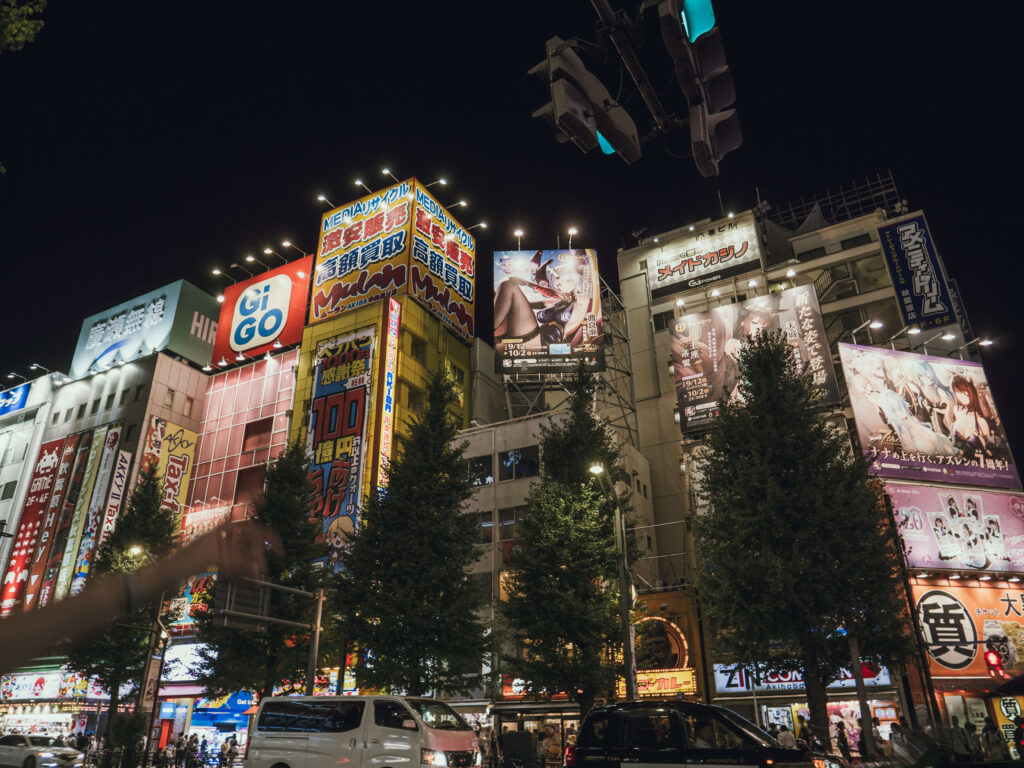 Façades lumineuses d’Akihabara la nuit, avec des enseignes colorées et des publicités sur des thèmes liés à l’animation et la culture otaku.