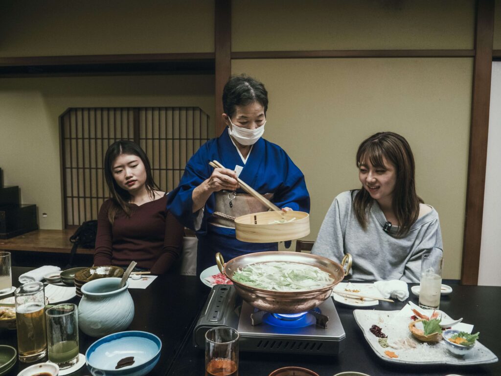 Repas traditionnel de shabu-shabu préparé par une hôtesse en kimono.